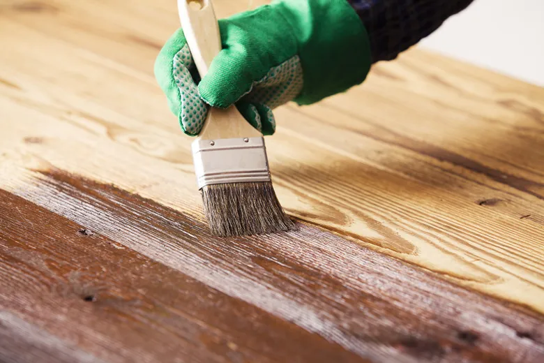 Applying smooth white enamel paint to a wooden cabinet door with a brush.