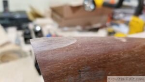 Close-up view of a damaged wooden gun stock showing a worn screw hole.