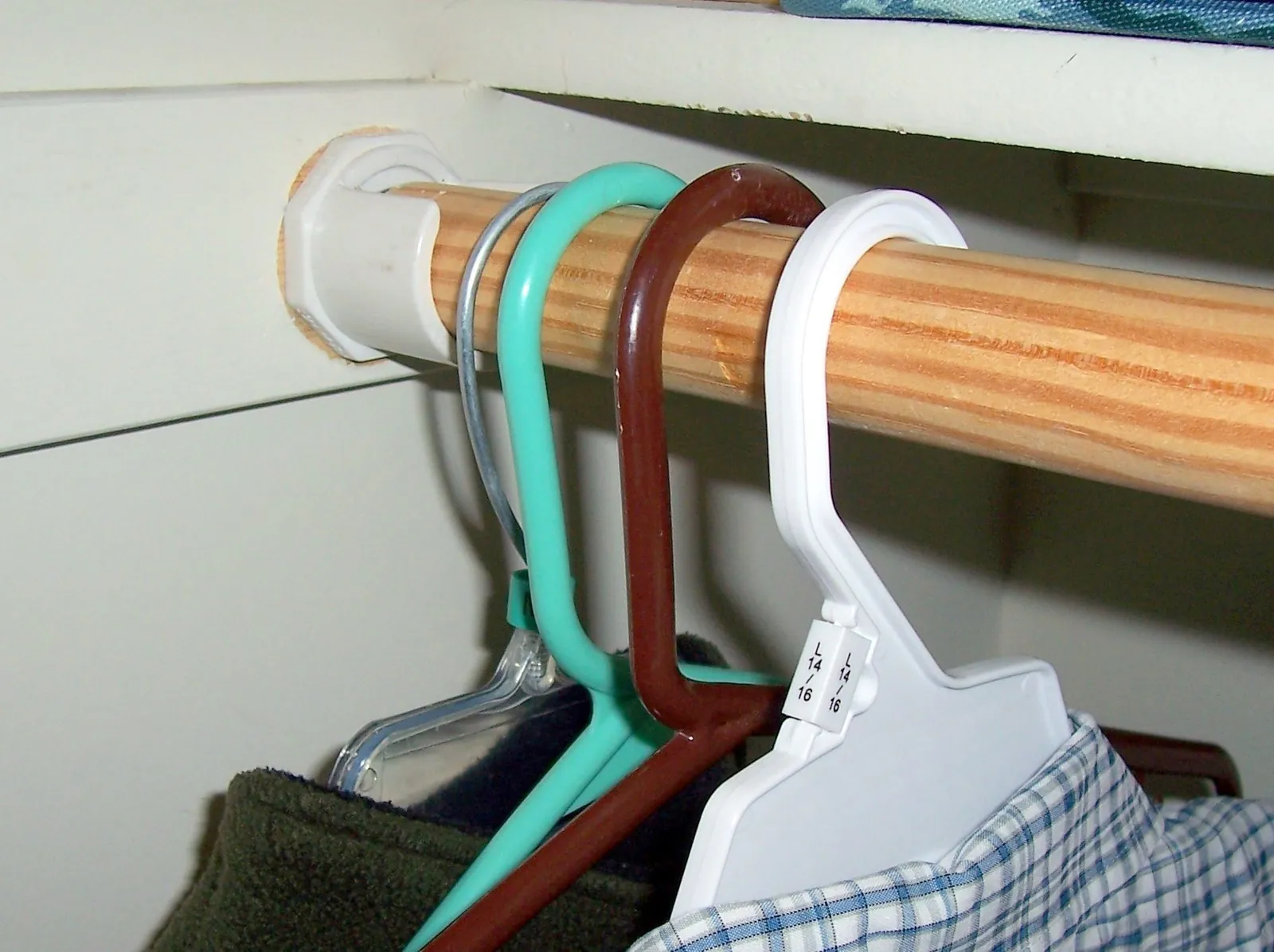 A close-up of a wooden closet rod showing slight sagging under heavy winter coats.