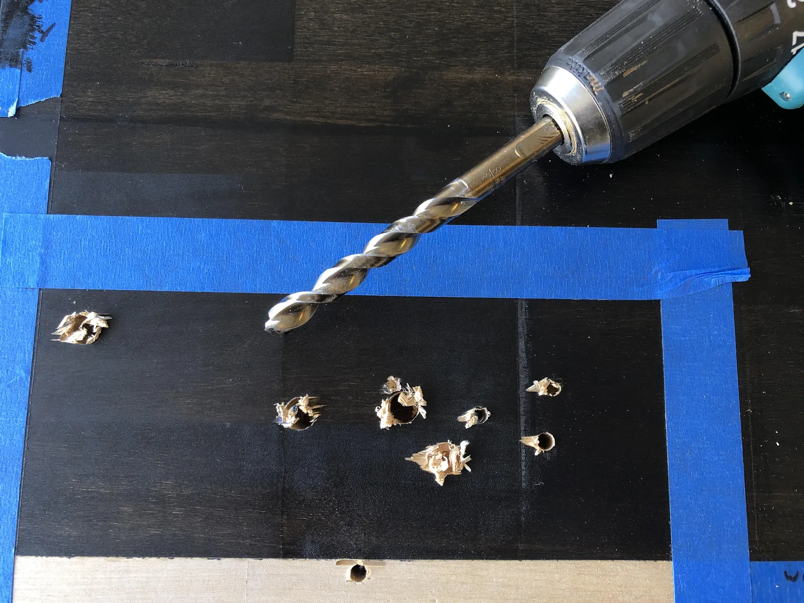 A drill bit pressing into hardwood with masking tape used to prevent wood splintering.