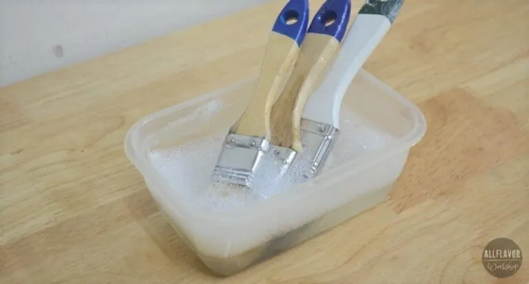 Rinsing a water-based polyurethane brush under a stream of warm water in a sink.