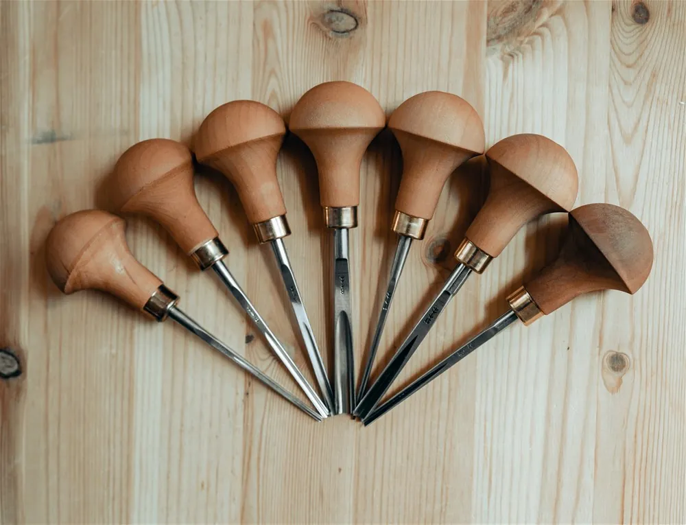 A series of sharpening stones arranged by grit progression next to a steel gouge.