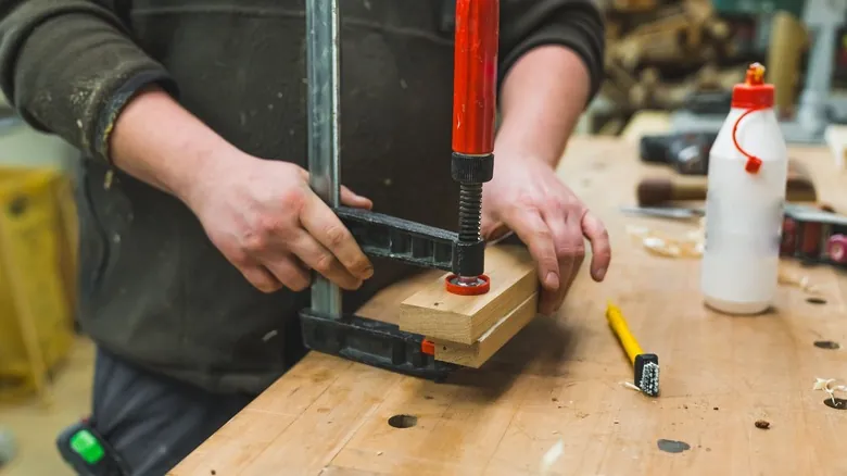 A woodworker using clamps to secure glued boards in a workshop.